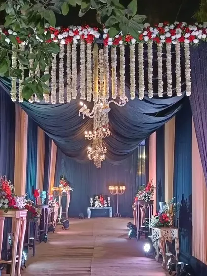 I create grand entrance passages that make guests feel special. This walkway uses dark drapes, elegant chandeliers, and fresh red and white flower arrangements to build excitement for the main event area.