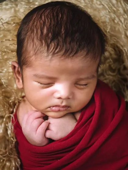The same baby in a classic pose, with hands gently tucked under the chin. The lighting is soft and focused, creating a timeless portrait.