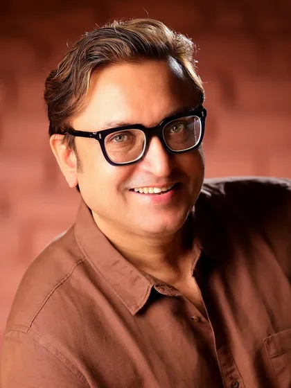 A warm and approachable portrait of Sanjev Sharma. This shot, with his glasses and smile, presents a friendly and intellectual character.