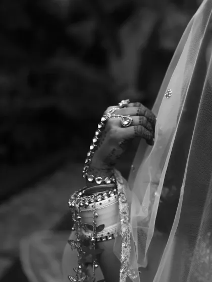 A classic black and white bridal detail shot, focusing on her hand, 'chooda' (bridal bangles), and veil.