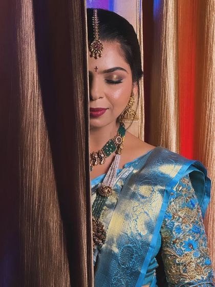 A creative shot of my bride Nishchitha, peeking from behind a curtain. Her Muhurtham look features a beautiful blue Kanjivaram saree with bold eyes and a bright red bindi.
