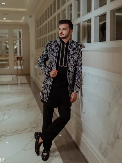 A confident, full-length portrait of the groom in his striking black and silver embroidered Sangeet jacket.