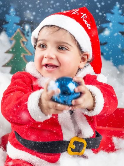 This baby Santa is fascinated by the shiny blue Christmas ornament.