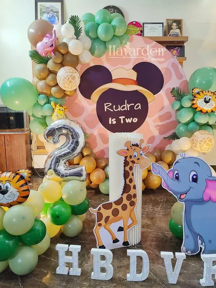 A fun and friendly jungle safari theme for a second birthday. This decor features a custom Mickey Mouse safari backdrop, lots of green and brown balloons, and cute animal cutouts like a giraffe and elephant. The large '2' foil balloon marks the special age.