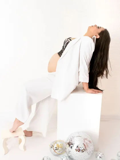 A powerful and artistic pose in a modern white suit. The mother-to-be arches back, creating a strong and graceful silhouette against a clean white background.