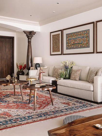 The living room is a comfortable and layered space, with a large traditional rug, framed Indian textiles, and an antique wooden pillar.