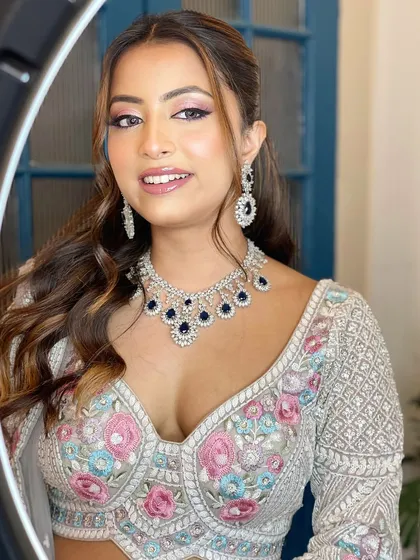 A smiling model showcases a beautiful zircon necklace with dark blue stones. Paired with a silver and pink embroidered blouse, this set is perfect for a wedding guest or bridesmaid.