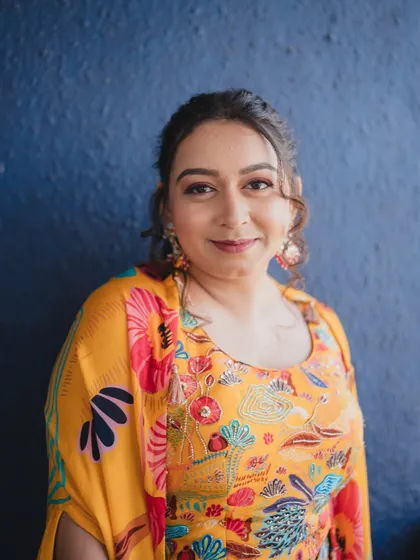 A portrait against a bold blue wall, making the colors of her outfit and makeup pop. The look is fresh, modern, and perfect for a daytime Mehendi party.