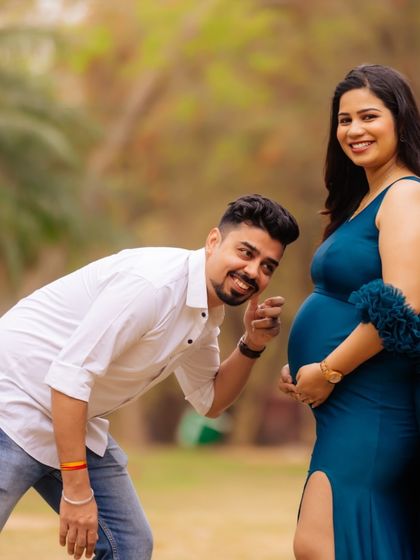 A fun and playful pose during an outdoor maternity shoot. The partner points to the baby bump with a smile, adding a touch of humor and excitement to the portrait.