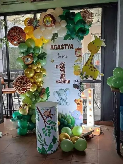 A cute jungle-themed first birthday decoration with a "Wild One" backdrop. The setup includes an organic balloon arch, animal cutouts, and a light-up number '1' for a fun safari vibe.