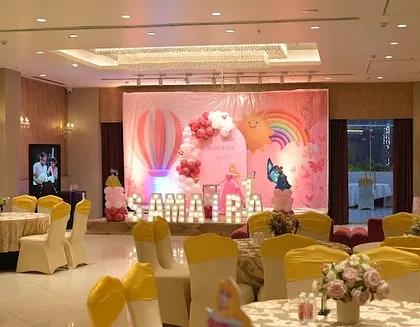 A wide view of the banquet hall, showing the main stage and the guest tables decorated with yellow chair sashes to match the princess theme.