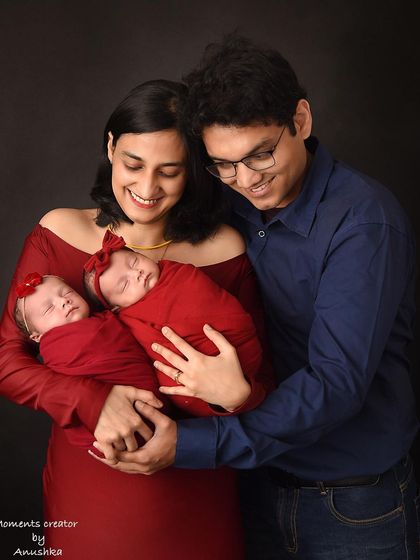 A heartwarming portrait of new parents with their twin baby girls. The coordinated red outfits and the parents' joyful smiles perfectly capture the love in this new family of four.