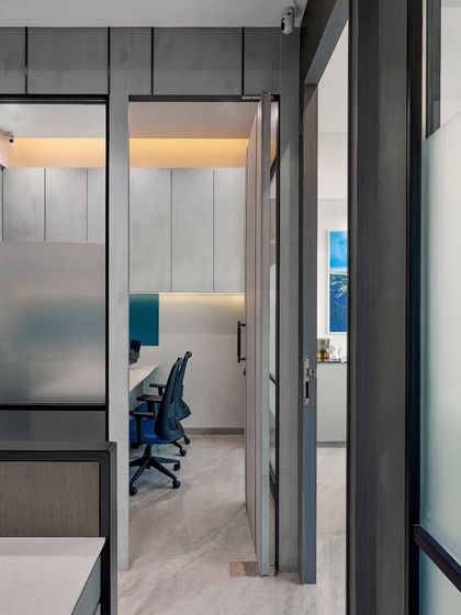 A view from the entrance into a modern workspace. The use of frosted and clear glass partitions maintains an open feel while providing necessary separation and soundproofing for focused work.