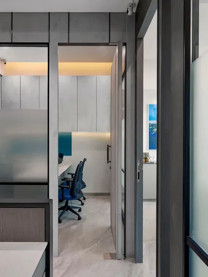 A view from the entrance into a modern workspace. The use of frosted and clear glass partitions maintains an open feel while providing necessary separation and soundproofing for focused work.