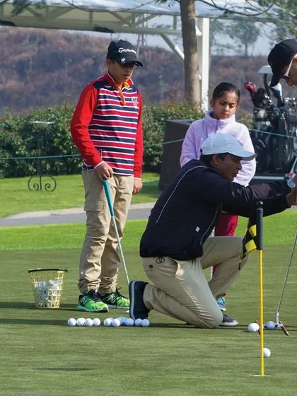 A coach provides hands-on instruction to junior golfers on the putting green, demonstrating our commitment to personalized lessons for every skill level.