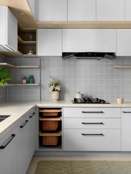 This kitchen features a soothing monochrome palette of grey and white, with open plywood shelving adding a touch of natural warmth. The design includes pull-out wicker baskets for accessible storage.