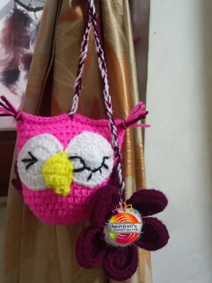 A wise and whimsical owl curtain tie-back in bright pink and purple. The sleepy-eyed owl is paired with a flower, adding a touch of nature to the design.