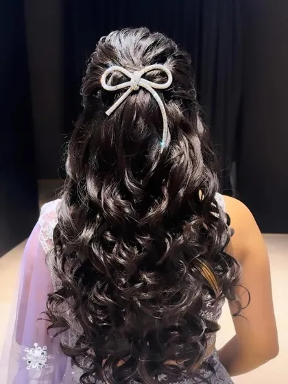 Hair goals! This half-up hairstyle with voluminous curls is finished with a sparkling bow accessory, creating a look that is both playful and elegant.
