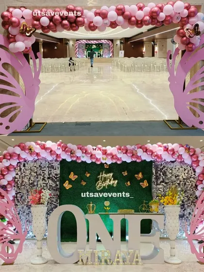A grand butterfly-themed entrance arch and stage setup for a first birthday. The large pink butterfly wings create a stunning welcome for guests.