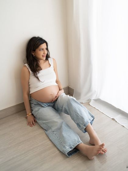 Simple, clean, and beautiful. A relaxed portrait of the mother-to-be sitting by the window, dressed in casual jeans and a white top for a modern maternity look.