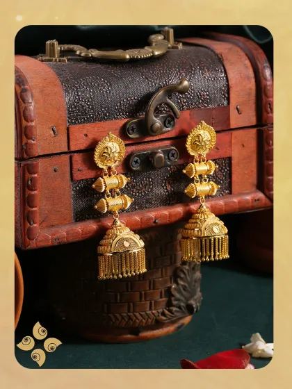 Elevate every look with our stunning gold jhumkis. These traditional earrings feature a classic bell shape with delicate fringe, set against a rich, antique-style background.