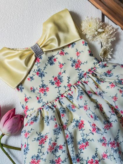 This dress is a burst of sunshine with its lemon-yellow satin collar and bow over a sweet floral print. The sequined ribbon on the bow adds just a hint of sparkle.