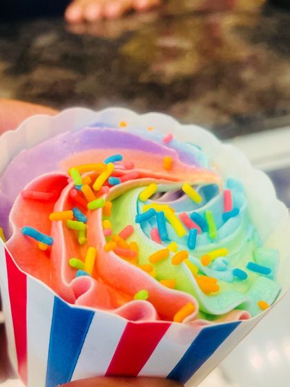 A hand-held shot of a rainbow cupcake, showcasing its vibrant colors in a striped red, white, and blue liner.