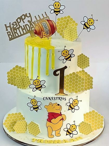 A sweet two-tier Winnie the Pooh cake for a first birthday. The design has a honey-drip effect and is decorated with cute bees and honeycombs.