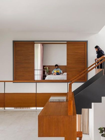 The 'Copper House' features a double-height void with a mezzanine library overlooking the lower level. Sliding louvered screens allow the bedroom to either open up to the central void or be closed off for privacy, creating a dynamic and adaptable living arrangement.