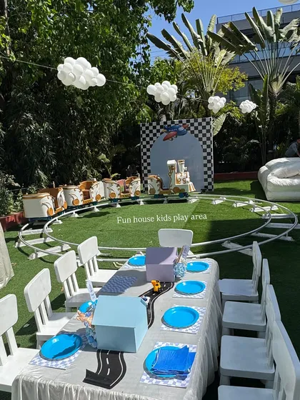 An outdoor party setup featuring our white tables and chairs with a car-themed table runner. In the background, our white train ride is ready to take the little guests on a fun adventure.