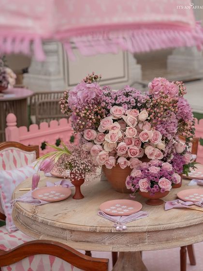 A dining table centerpiece bursting with pink and purple flowers, set under a classic fringed garden umbrella.