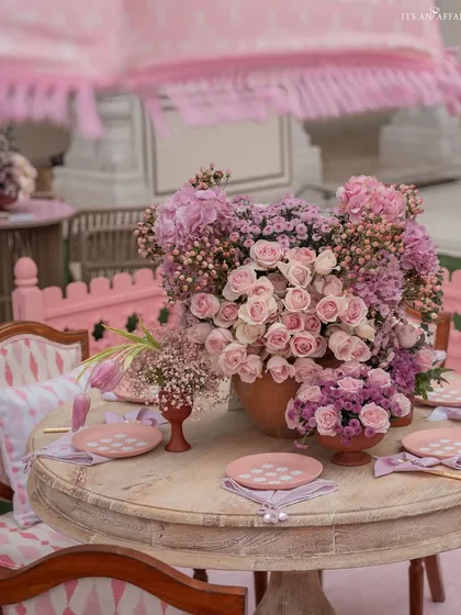 A dining table centerpiece bursting with pink and purple flowers, set under a classic fringed garden umbrella.