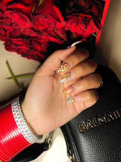 Glamorous and artistic nails. This design features a unique, hand-painted flame-like pattern in warm tones, perfectly complementing the client's traditional red bangles.