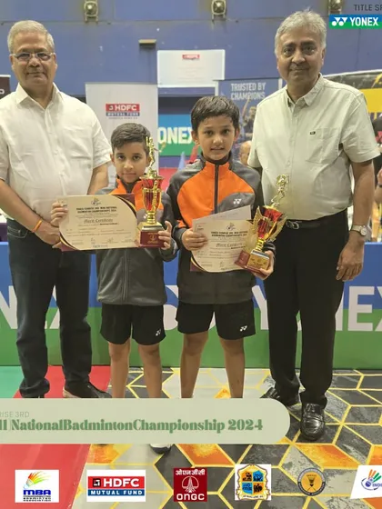 Two young boys proudly displaying their trophies at the Mini National Badminton Championship.