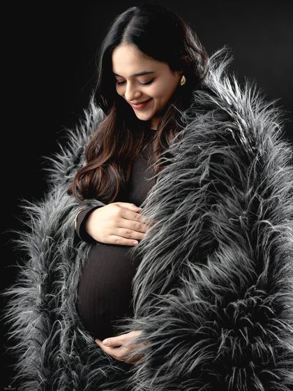 A cozy and stylish portrait. The mom-to-be is wrapped in a luxurious faux fur throw, adding texture and warmth to this intimate black and white shot.