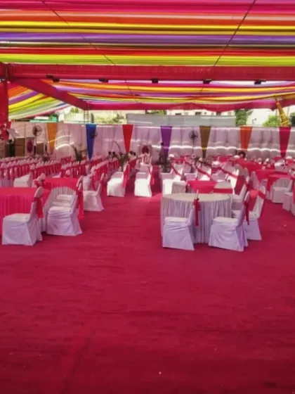 A large pandal setup with a colorful striped fabric ceiling and neatly arranged round tables with pink covers for a massive wedding lunch.