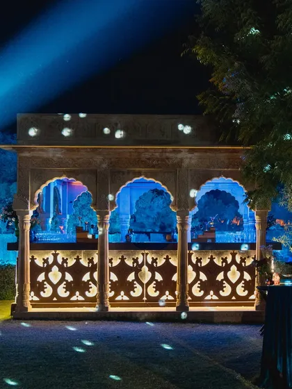 A beautifully lit architectural pavilion at night, with patterned jaali work creating intricate shadows, showcasing how we use light to enhance a venue's features.