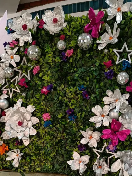 A photo backdrop should be a work of art. I designed this chic and modern photo wall using a lush green foliage base, accented with oversized, handcrafted paper flowers and sparkling disco balls for a touch of glamour.