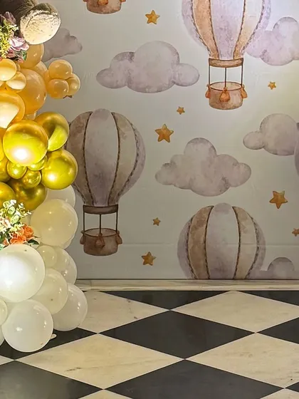 The custom-printed backdrop featuring a pattern of hot air balloons, clouds, and stars, which forms the base of the photo booth's theme.