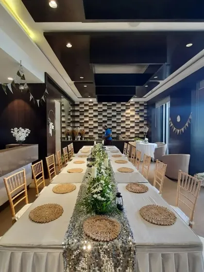 An elegant long-table dinner setup, perfect for an intimate gathering. The table is decorated with a sequin runner and a beautiful floral centerpiece.