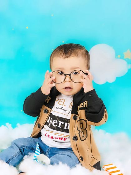 A baby boy tries on a pair of glasses, looking like a curious little intellectual in his sky-themed photoshoot.