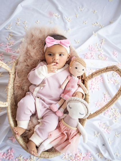 Celebrating six months of cuteness. This baby girl is dressed in pink, holding her dolls in a cozy basket.