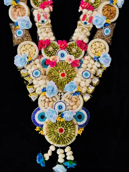 An elaborate dry fruit and chocolate garland with an evil eye theme and blue flowers, making it a grand festive gesture.
