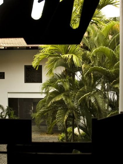 A view of the LMW Headquarters courtyard framed by a custom metal screen. The abstract pattern of the screen creates a dynamic interplay of light and shadow, filtering the view of the lush greenery beyond.