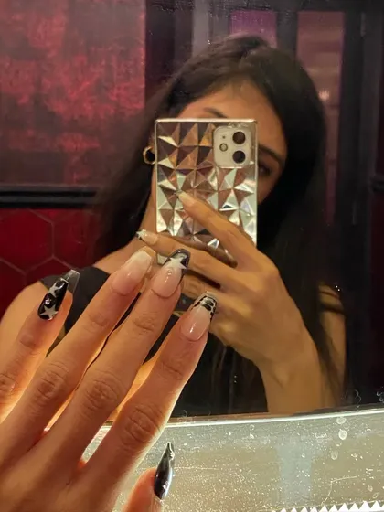 Chase your dreams in a killer pair of heels and perfectly painted nails. A mirror selfie showing off these long, black party nails with star and checkerboard art.