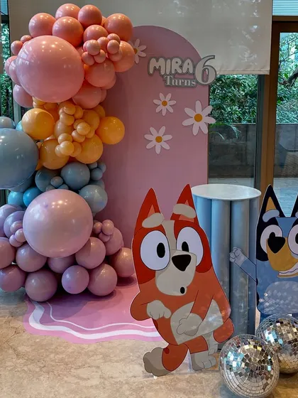The main photo backdrop for the Bluey-themed party, with large character cutouts, disco balls for a touch of sparkle, and a vibrant organic balloon arch.