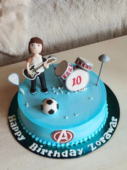 A cake for a multi-talented 10-year-old, decorated with a fondant figure playing guitar, a drum set, and a soccer ball.