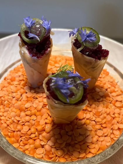 Miniature savory cones filled with a beetroot tartare and topped with pickled elements and edible flowers. A visually striking and flavorful start to a meal.