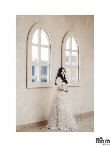A beautiful solo portrait of the bride standing by arched windows, her elegant white lehenga perfectly complemented by the minimalist architecture.