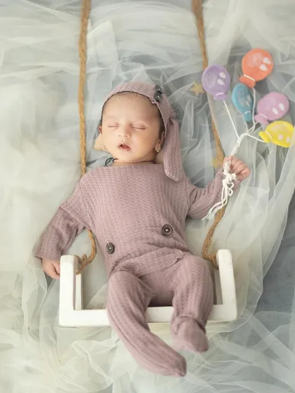 Drifting off to dreamland on a tiny swing, holding a bunch of miniature balloons. This whimsical setup adds a touch of fantasy to the newborn portrait.